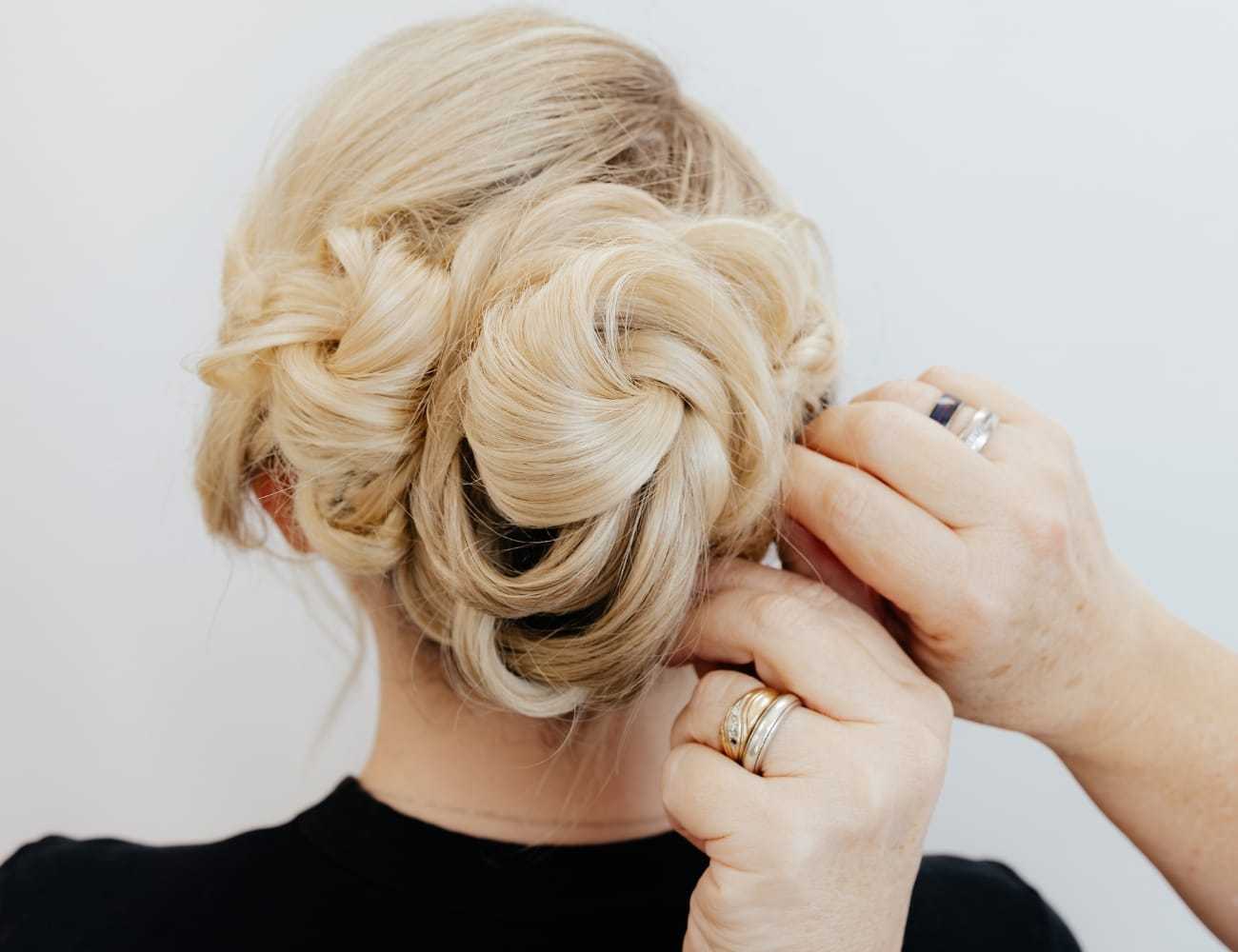 Elegant braided updo styled by hands against a neutral background.