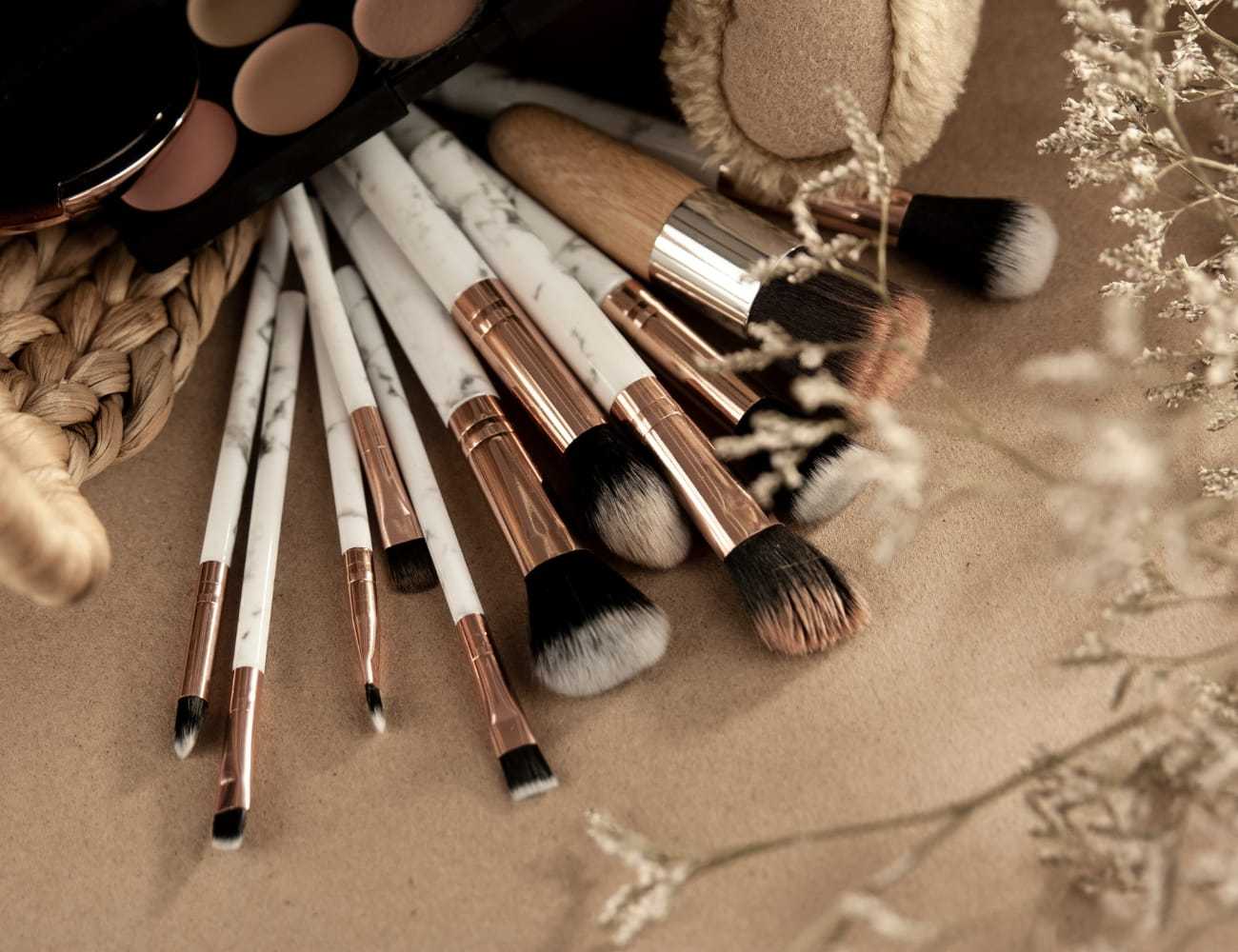 Makeup brushes with marble handles on a beige surface, surrounded by dried flowers.
