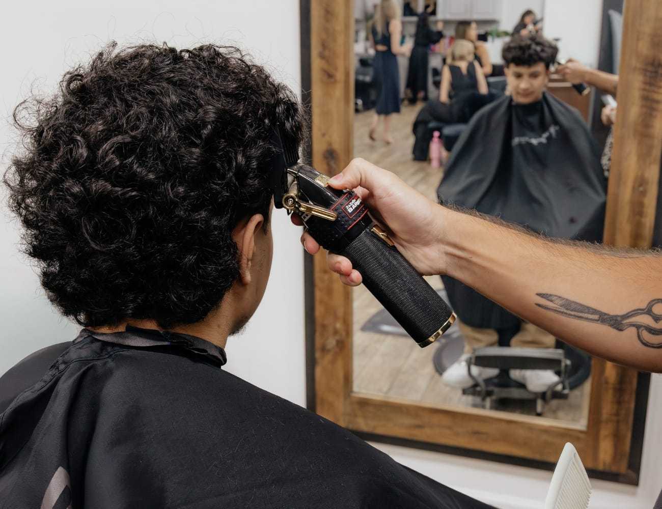 Person gets haircut at salon, reflected in mirror.