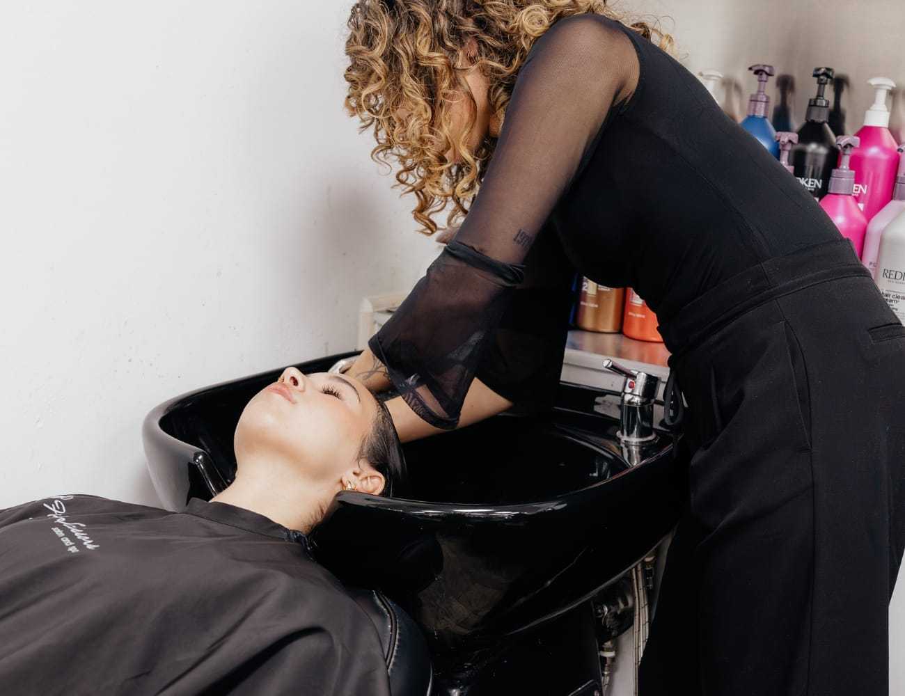 Salon worker washing woman's hair at shampoo station.