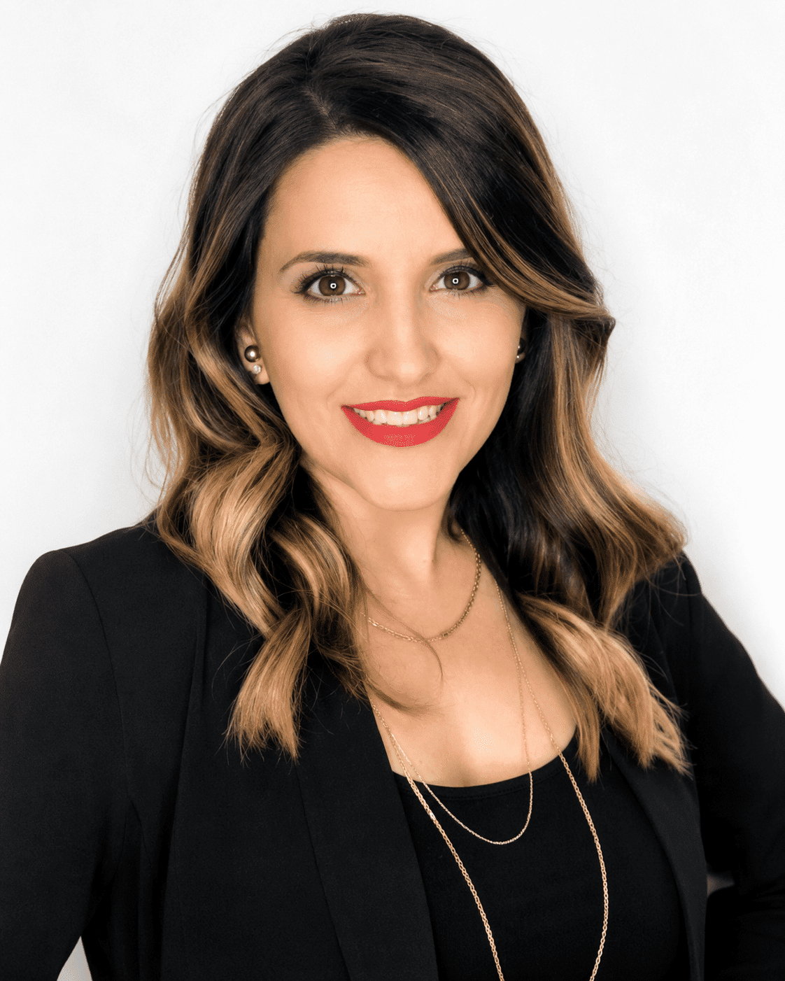 Portrait of a woman with wavy hair, wearing a black blazer and red lipstick, smiling.