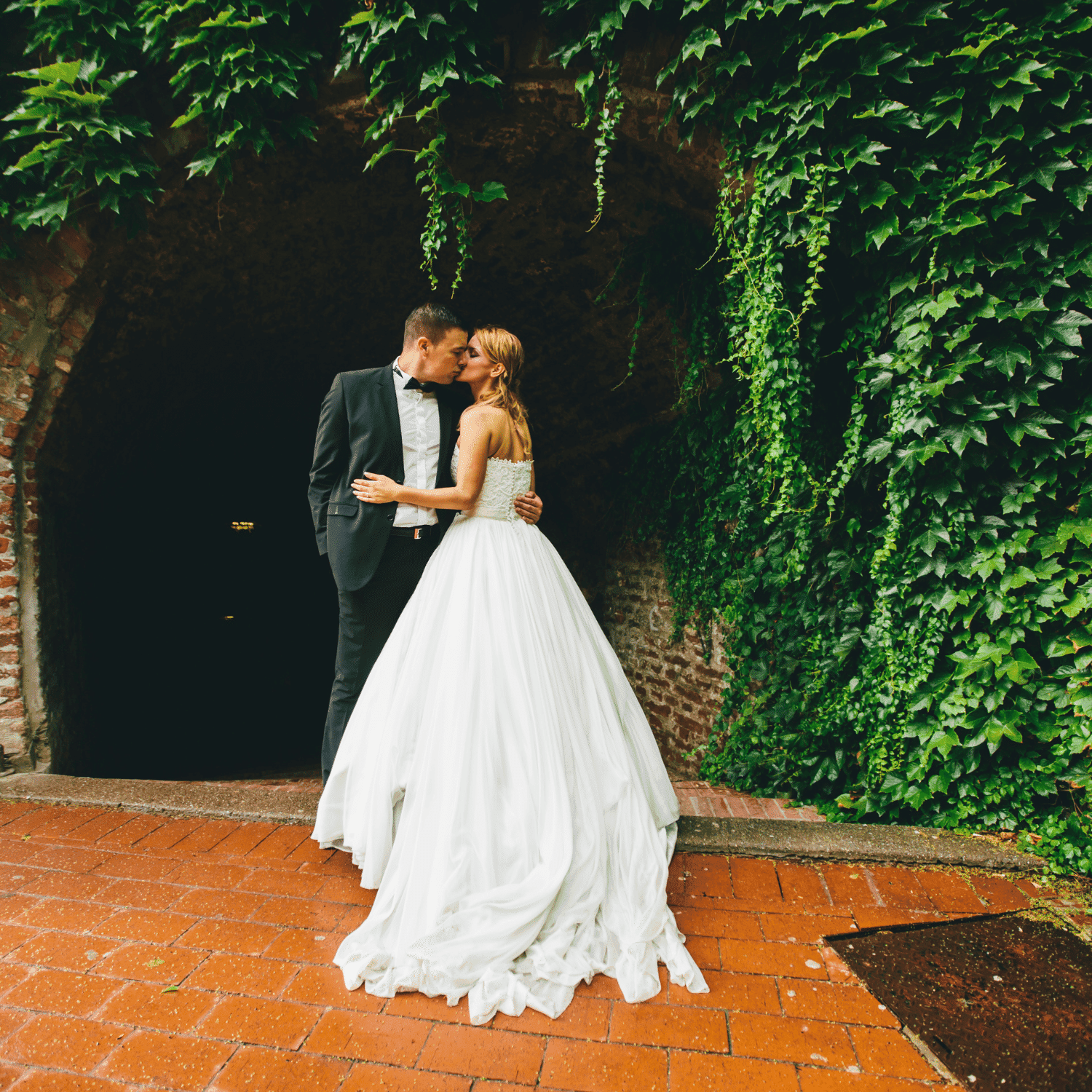 Bride and groom share a kiss, surrounded by lush ivy.